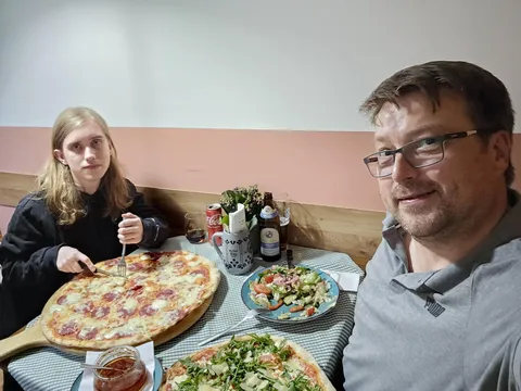 Jan und Jürgen sitzen am Tisch im Restaurant und jeder hat eine große Pizza vor sich auf dem Tisch